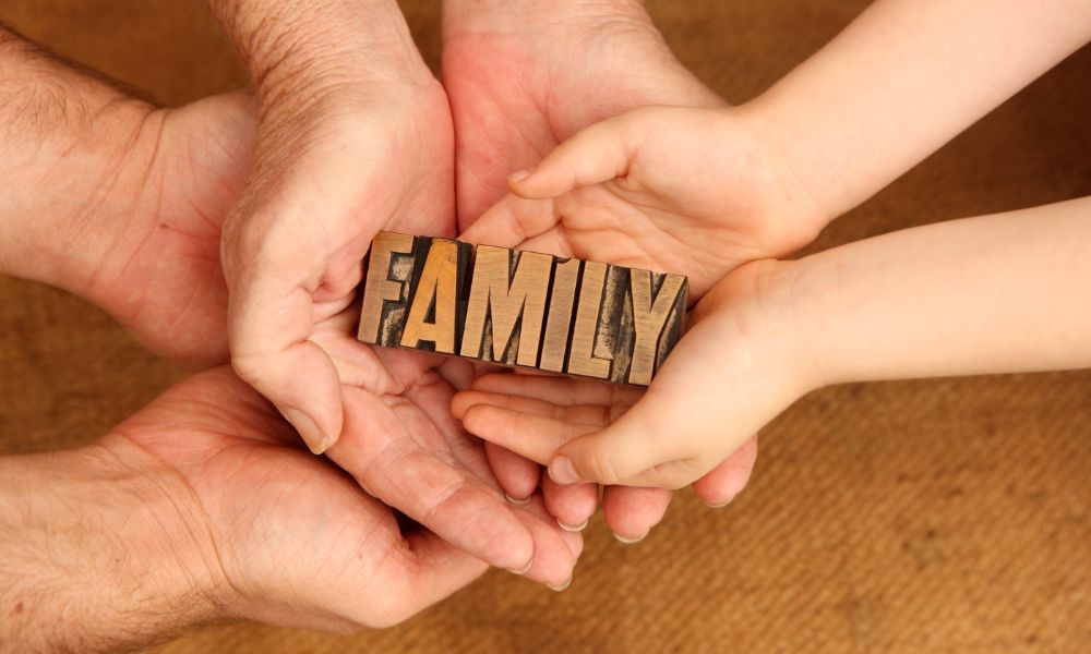 Hands of a father, mother, and child holding a wooden family sign to illustrate telling their story.