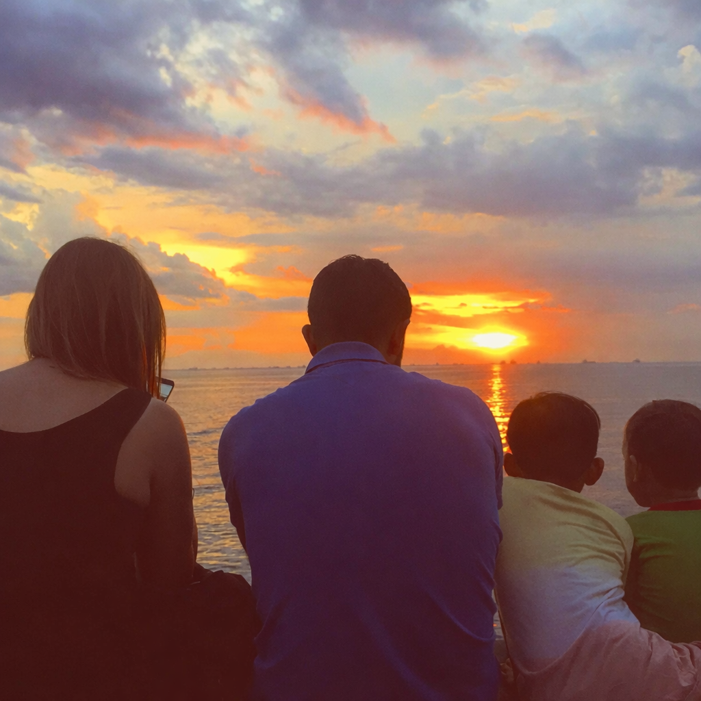 A family sitting together on a hill, watching the sunset over the horizon, symbolizing simple living, togetherness, and quality family time.