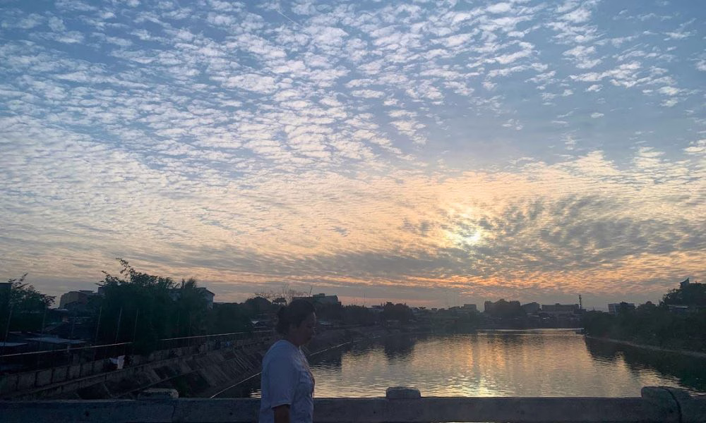 A woman walking on the bridge over the river on a sunrise in Davao City.